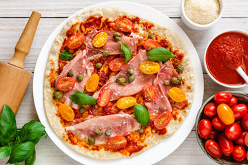 Italian pizza with prosciutto ham, capers, cherry tomatoes, parmesan cheese and decorated with basil leaves.