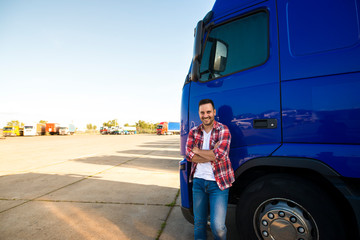 Portrait of smiling trucker standing by his truck ready for driving. Driver occupation....
