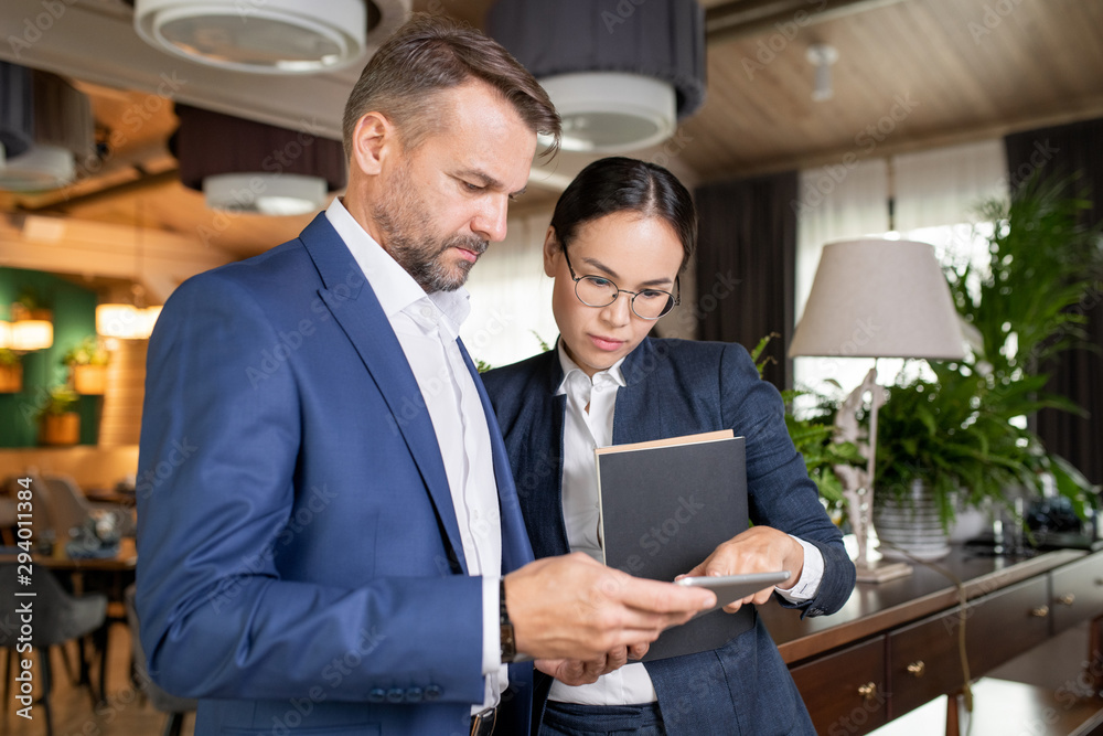 Poster two serious colleagues in formalwear reading electronic document in touchpad