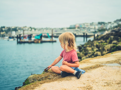 Little toddler sitting by the harbor