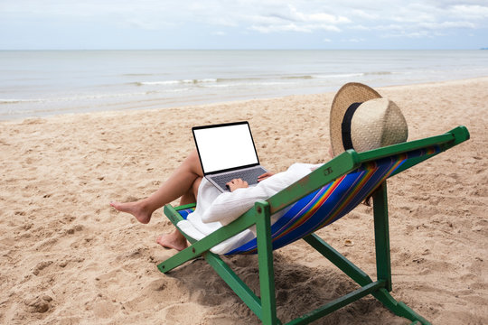 Mockup image of a woman using and typing on laptop computer with blank desktop screen while lying down on a beach chair