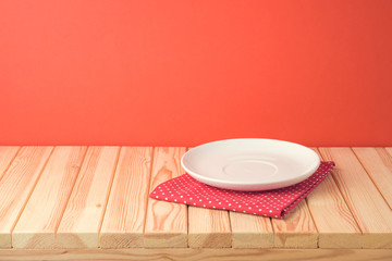 Christmas wooden table with empty plate and tablecloth over red festive background