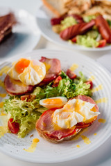 Toasts with ham, tomato and poached egg, served with fresh salad on white plate. Healthy breakfast on the table in the restaurant. Close-up. Space