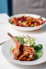 Tobacco chicken with salad on a white table in a restaurant. Tea and dessert on a blurred background. Large plna. Space