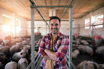 Fototapeta na wymiar Portrait of happy farmer with crossed arms standing in pigpen taking care of pigs domestic animals.