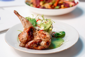 Tobacco chicken with salad on a white table in a restaurant. Tea and dessert on a blurred background. Large plna. Space