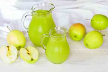 freshly squeezed apple juice in glass jugs and green apples on a white background. Apple juice and apples closeup.