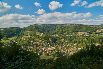 Aerial view on small village in Czech republic hills. Green hill forests and blue sky with white clouds
