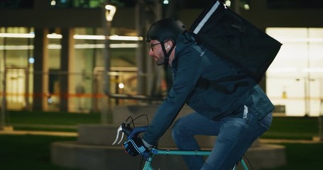Slow motion of an young delivery courier with bicycle is touching a futuristic screen with augmented reality hologram maps to view the addresses of customers in the evening in a city center. - Powered by Adobe