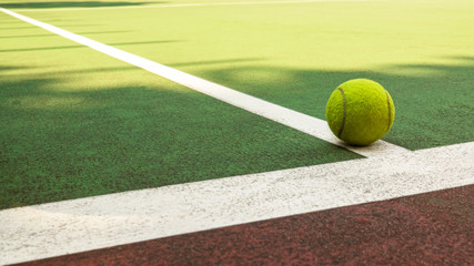 Yellow tennis ball hitting the sidelines on an green and orange artificial tennis court in the afternoon sun. sport background