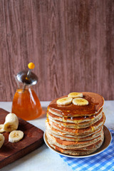 Fototapeta na wymiar Pancakes with banana,walnut and muple syrup for a breakfast on wooden background closeup. Copy space. Vertical...