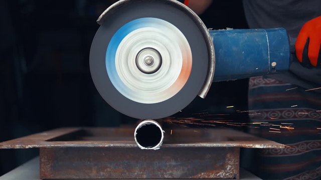 Angle grinder cutting through rusty iron pipe, close up, sparkles