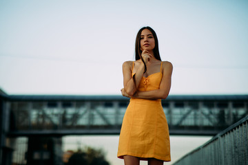 Woman stands on a background of a bridge and sky.