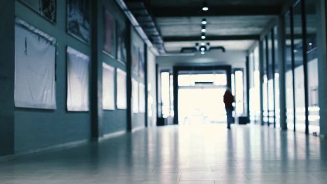Silhouette of a person walking out a dim gallery building or business center corridor, blurry low angle view