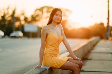 A woman sits on the sidewalk on a background of cityscape at sunset.