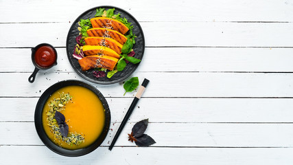 Pumpkin dishes in black plate on white wooden background. Autumn dishes. Top view. Free space for your text.