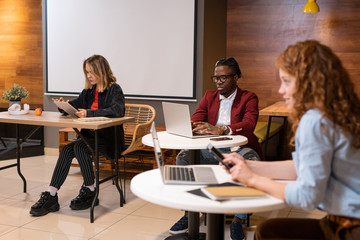 Fototapeta premium Group of young intercultural students of college sitting by tables in cafe