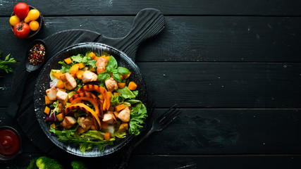 Pumpkin salad with chicken meat and vegetables in a black plate on a black background. Top view. Free space for your text.