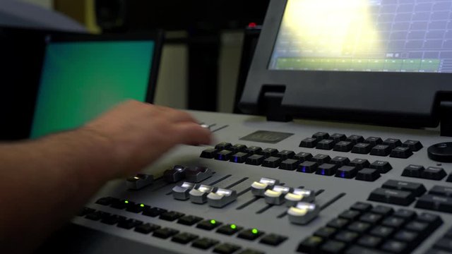 Light or sound engineer is moving levers of a multitrack mixing console in the control room during a recording session