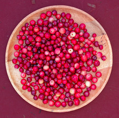 Ripe red cranberries on a wooden tray on a textured Burgundy background. Useful berry to improve health, maintain immunity in the season of colds. Folk medicine