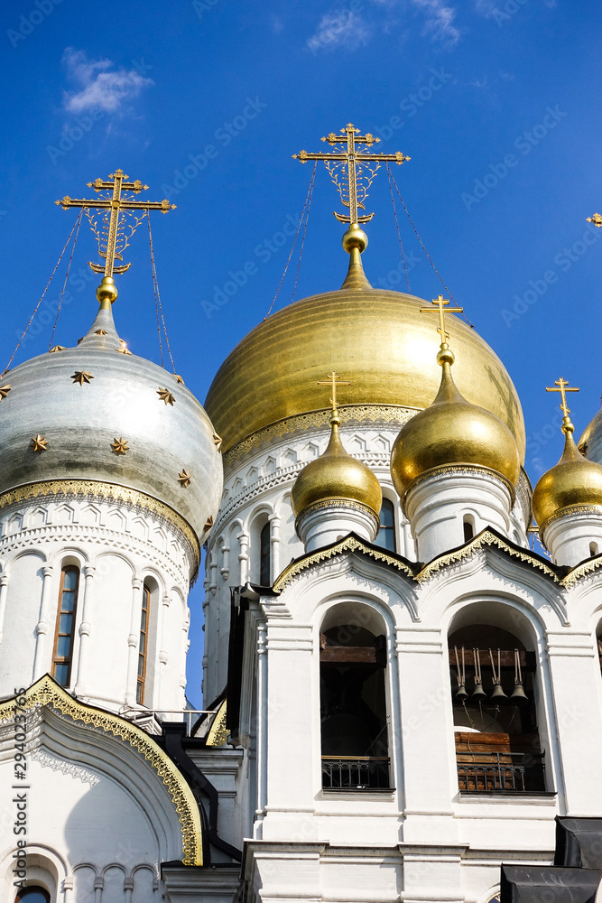 Wall mural Golden domes with crosses of an orthodox temple on the background of bright blue sky. Snow-white facade. Christian faith.