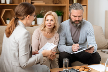 Mature woman consulting with real estate agent while her husband reading paper