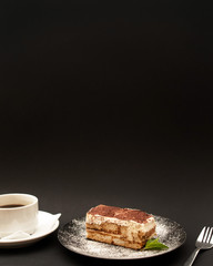 Vegan Tiramisu cake with a cup of coffee on a black background.