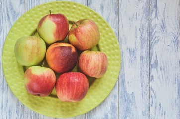 Fresh red fruits. Apples on a green plate on a wooden background.