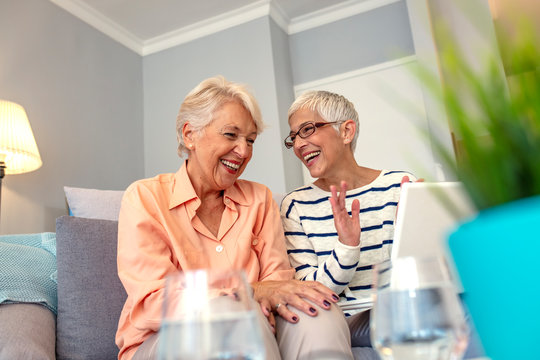 Joyful Female Friends Having A Conversation. Senior Women Socializing In Lounge Using Laptop Computer At Senior Care Center. Social Seniors. Portrait Of Two Beautiful Senior Women