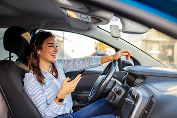 Portrait of a young woman texting on her smartphone while driving a car. Business woman sitting in...