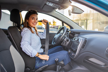 Young girl is fastening her seat belt. Photo of a business woman sitting in a car putting on her seat belt.  Woman fastening seat belt in the car, safety concept - obrazy, fototapety, plakaty