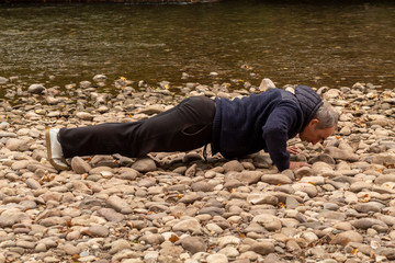 Middle Age Men Doing Push Ups on Rocky Ground Near River