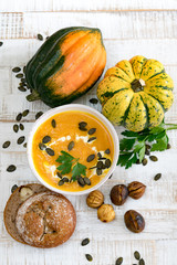 organic pumpkin soup in a white bowl framed by chestnuts pumpkins parsley and chestnut bread