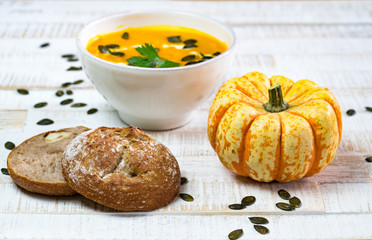 Naklejka na ściany i meble organic pumpkin soup in a white bowl framed by pumpkin and chestnut bread and pumpkin seeds