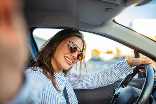 Road trip selfie. Young woman using her smartphone and making selfie while driving a car. Young woman taking selfie picture with smart phone camera in car. Smiling young woman taking selfie picture