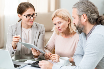 Confident young agent with touchpad pointng at electronic document on display