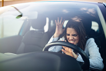 Closeup portrait, angry young sitting woman pissed off by drivers in front of her and gesturing with hands. Road rage traffic jam concept. Woman is driving her car very aggressive