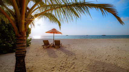 Beautiful tropical sunset scenery, two sun beds, loungers, umbrella under palm tree. White sand, sea view with horizon, colorful twilight sky, calmness and relaxation. Inspirational beach resort hotel