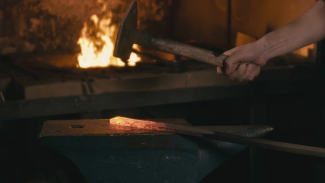 Forge workshop. Smithy manual production. Hands of smith with hammer hit on glowing hot metal, on the anvil, the forging process.