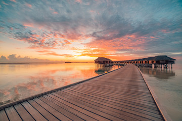 Amazing sunset panorama at Maldives. Luxury resort villas seascape under colorful sky. Exotic travel destination, luxurious vacation