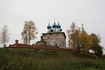 Fototapeta premium Old church in russia among yellow birch trees in cloudy day