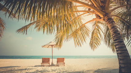 Beautiful tropical sunset scenery, two sun beds, loungers, umbrella under palm tree. White sand, sea view with horizon, colorful twilight sky, calmness and relaxation. Inspirational beach resort hotel