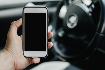 A telephone with a blank display on the background of the steering wheel and dashboard. The man is...