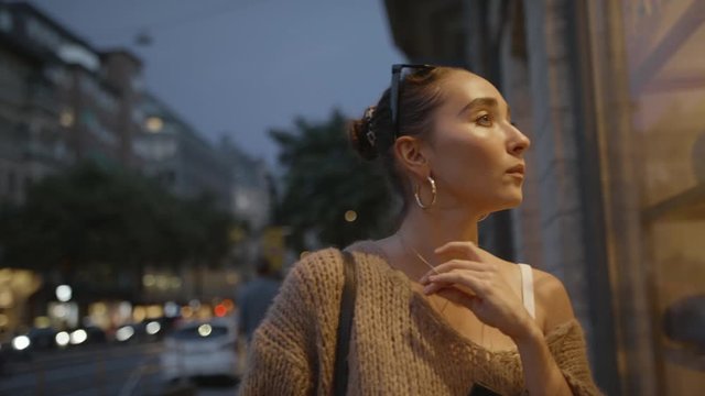 A young shopaholic woman looking through a shop window and nervously touching her necklace