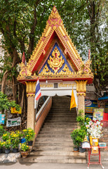 Si Racha, Thailand - March 16, 2019: Red, gold, blue gate on stairway to Wat Koh Loy Buddhist shrines on the hill of Ko Loi Island with gren foliage. Donation box at bottom.