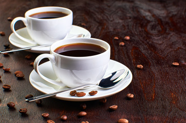 coffee on dark backgroundTwo cups of coffee in a saucer and coffee beans on a dark wooden table.