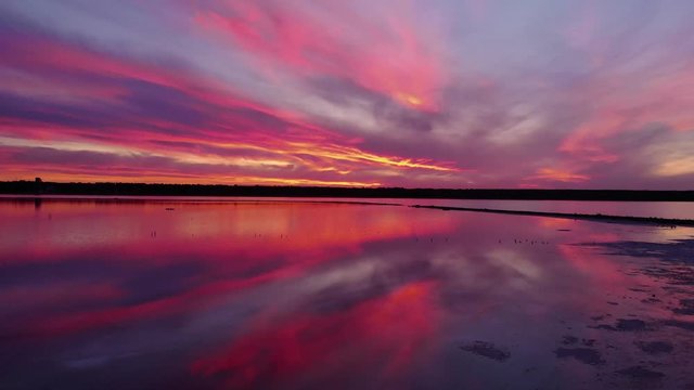 Aerial view of drone slide over water surface in twilight, golden hour sunset. Cinematic shot camera flies over calm firth surface reflecting majestic red and pink clouds