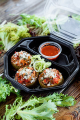 Meat balls with fresh lettuce and red sauce in a black eco container on a wooden rustic background among fresh herbs. Food delivery. Space. Take with you