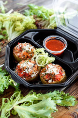 Meat balls with fresh lettuce and red sauce in a black eco container on a wooden rustic background among fresh herbs. Food delivery. Space. Take with you