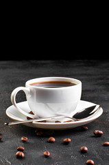 A Cup of coffee on a saucer and coffee beans on a dark background.